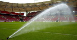 Wasserstrahl aus einer Beregnungsanlage auf dem Rasen eines Fußballplatzes